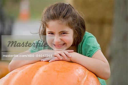 Little Girl Smiling on Top of a Big Pumpkin