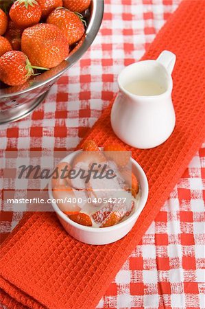 Sliced strawberries with cream in a white pot on a red cloth