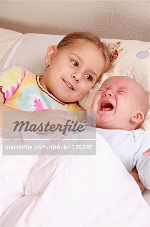 Cute older sister with crying newborn in bed