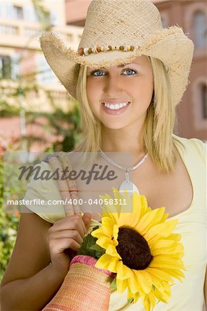 A beautiful young blond woman wearing a straw cowboy hat carrying a shopping bag of sunflowers