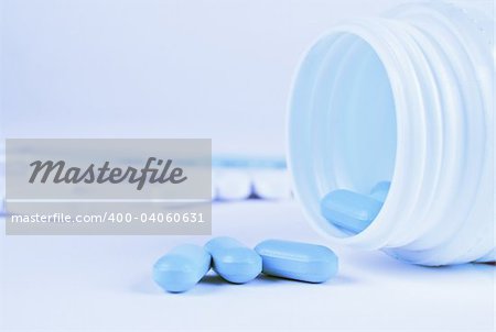 Pills spilling from prescription bottle in blue lighting