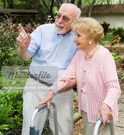 Senior couple taking a walk outdoors together.  She's using a walker.