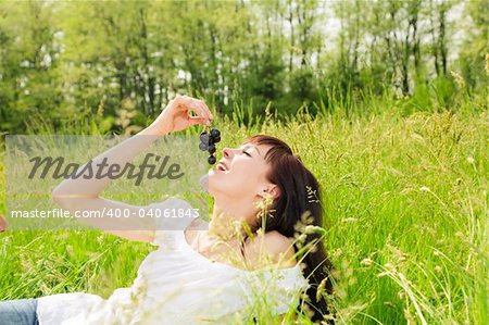 beautiful girl lying down of grass, eating black grapes. Copy space