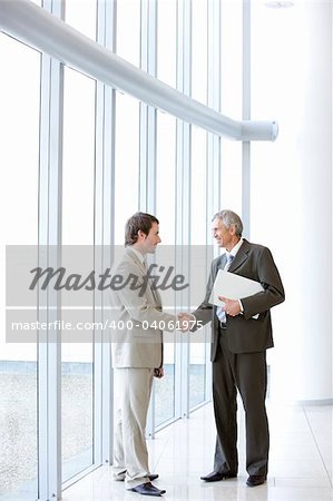 Two business men standing in a modern office building shaking hands