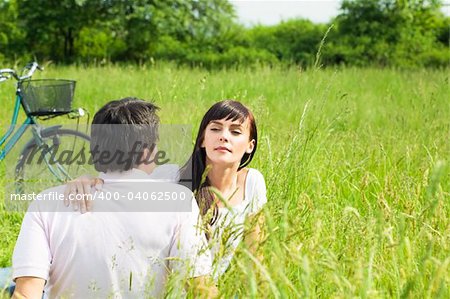 Young couple outdoors sitting in meadow, woman looking around. Copy space