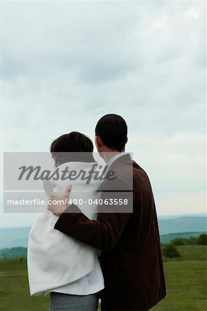 Couple looking at a green grass and the sky holding each other