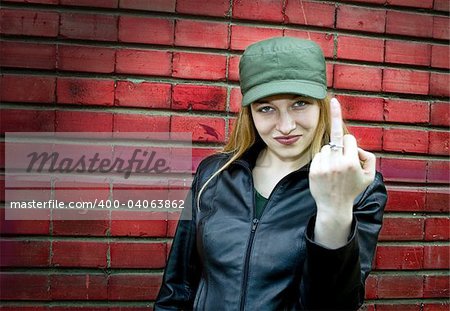 Aggressive young woman showing middle finger (brickwall as background)