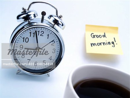 An alarm clock, a cup of fresh coffee and a yellow note with this text: 'Good morning!'