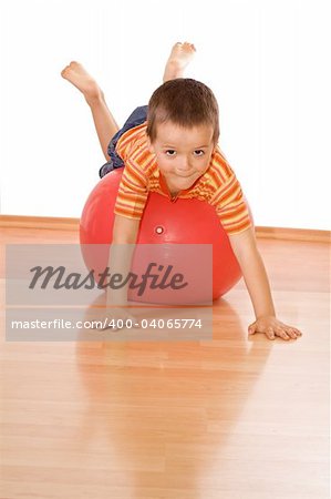 Little boy playing with a huge red gymnastic ball