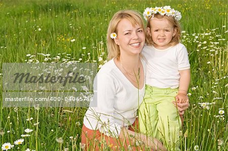 Happy mother with daughter sitting on the meadow full of daisies