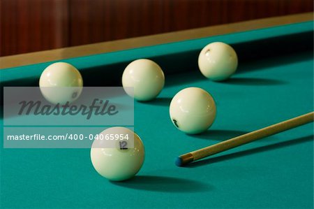 Five white billiard-balls and a wood cue on a green table