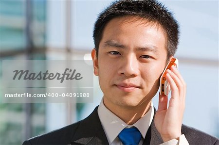 Good looking asian business man standing with formal suit and mobile phone.