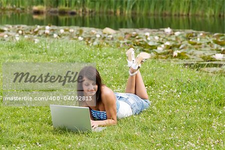 cute brunette in casual dress standing alone on the grass and working on the computer