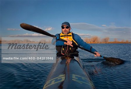 mature paddler exercising in a narrow carbon fiber racing kayak on a lake in early spring in Colorado, thirteen - temporary race number placed on deck by myself