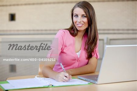 Girl wearing pink studing at table with silver laptop.