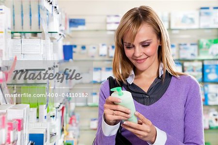Portrait of blonde woman reading label of shampoo in pharmacy. Copy space