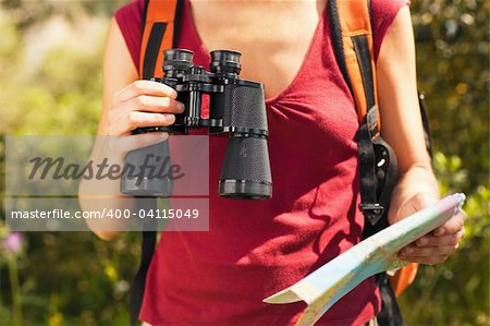 cropped view of female bird watcher holding binoculars and map.