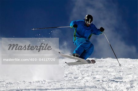 Skier jumping on a slope against blue sky.