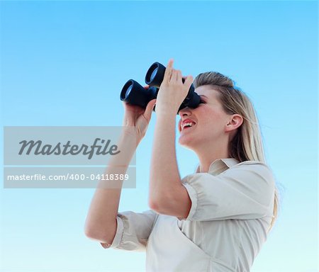 Blonde businesswoman looking through binoculars against blue sky