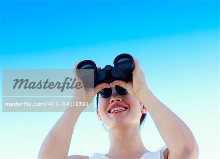 Smiling businesswoman looking through binoculars against blue sky