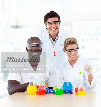 Scientists examining test-tubes in a laboratory smiling at the camera