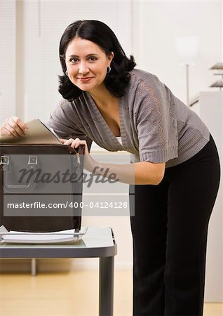 Attractive brunette searching in briefcase, looking at camera. Vertical