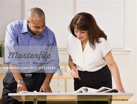 A businessman and woman are working together in an office.  They are looking away from the camera.  Horizontally framed shot.