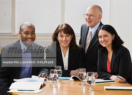 Four business workers, two men and two women, sitting at desk smiling at camera. Horizontal