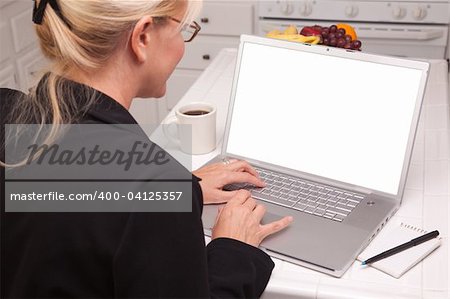 Woman Sitting In Kitchen Using Laptop with Blank Screen. Screen can be easily used for your own message or picture using the included clipping path.