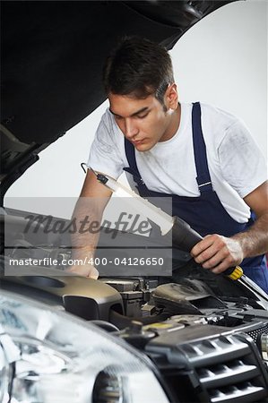 mechanic looking to car engine and holding lamp