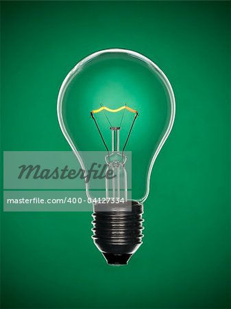 A transparent light bulb over a green background. Tungsten glowing filament.