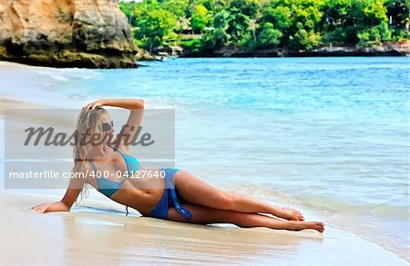 Blond girl in sunglasses lying on the beach with reflection in water