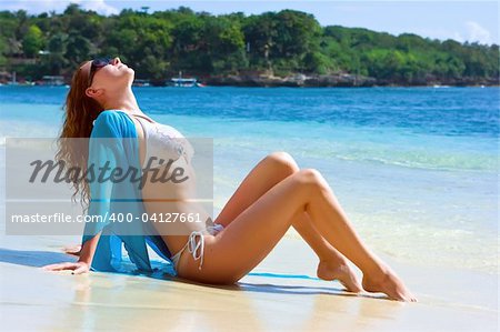 Beautiful brunette young girl relaxing on the sand beach on Bali island in Indonesia