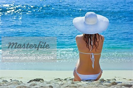 Belle brune aux cheveux longs en chapeau blanc et maillot de bain se trouve sur la plage de sable de l'océan sur Bali en Indonésie
