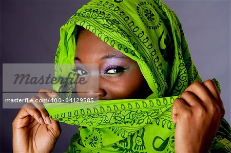 The face of an innocent beautiful young African-American woman covering her mouth with green headwrap and purple-green makeup, isolated