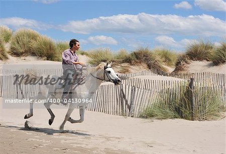 junger Mann und seinem weißen Pferd im Galopp am Strand
