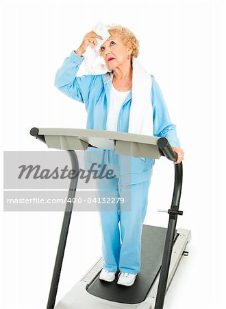Senior lady on a treadmill mops sweat from her forehead with a towel.  She doesn't like working out.  Isolated.