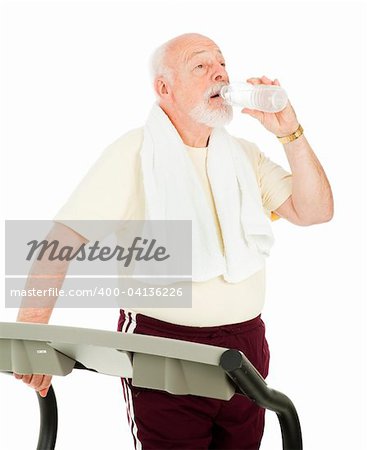 Senior man on treadmill takes a break to drink from a water bottle.  Isolated on white.