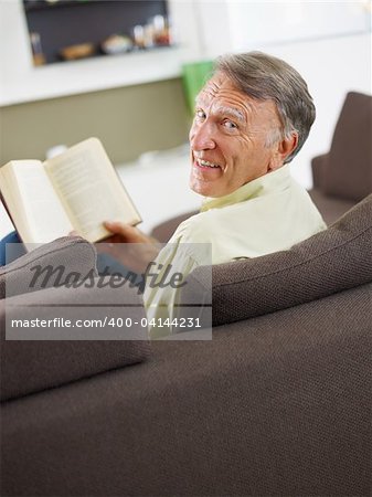 senior man reading book at home and looking over shoulders