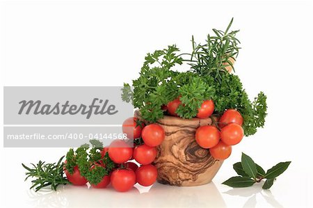 Tomatoes with rosemary, parsley and bay leaf herbs in an olive wood mortar with pestle, over white background with reflection.