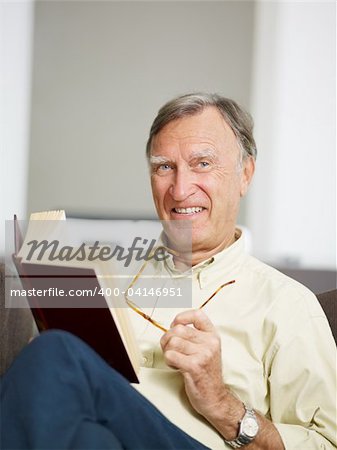 senior man reading book at home and looking at camera. Copy space