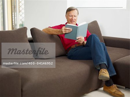 senior man reading book at home and smiling