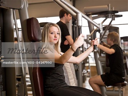 Girl using an exercise machine at a health club with two men in the background