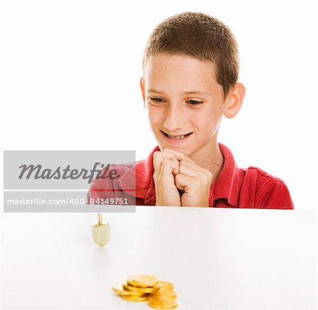 Boy watching a Hanukkah dreidel spin, with chocolate gelt in the foreground.  Isolated on white.