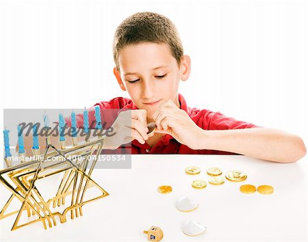 Little boy playing with his dreidel and eating chocolate coins on Chanukah.  White background.