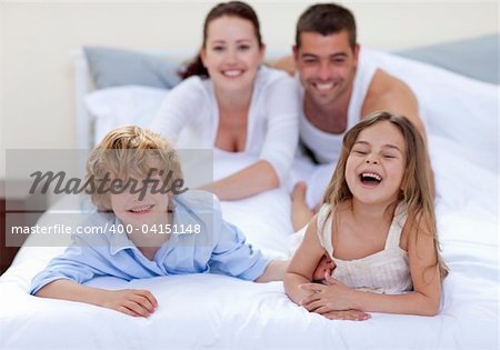 Happy brother and sister having fun in bed with their parents