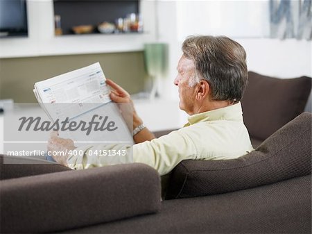 senior man sitting on sofa and reading newspaper