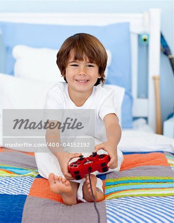 Little boy playing videogames sitting in his bed