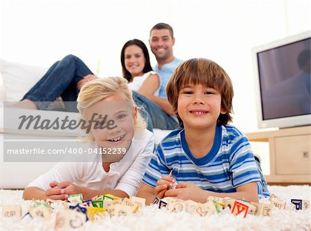 Brother and sister playing with alphabet cubes at home with parents on sofa