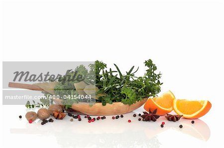 Herb leaf and spice selection with an olive wood bowl and two orange halves over white background with reflection.